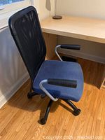 Side view of black mesh backrest and blue cushioned seat of Ikea office chair with armrests and caster wheels.