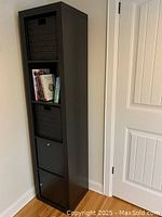 Full view of tall black-brown shelf unit with two black woven baskets and two black inserts with doors in a hallway corner.