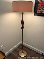Full view of floor lamp showing teak and brass body with fabric shade, positioned in corner of room.