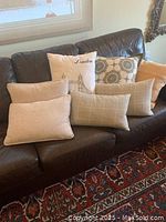 View of 7 designer pillows arranged on a dark leather couch showing variety of colors and textures.