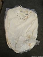 White ladies blazer/jacket still wrapped in plastic, lying on a dark surface.