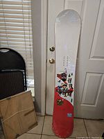 Full front view of the snowboard leaning against a door showing the overall design and condition