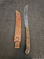 Machete and leather sheath laid out side by side showing full length and handle details.