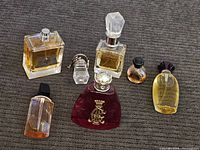 Overall view of seven perfume and cologne bottles, varying sizes and shapes with liquids between 50-80% full except one small bottle empty.