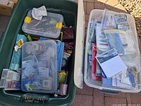 Photo of two large plastic totes, one green filled with smaller containers holding jewelry supplies, one clear containing assorted craft papers.