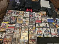 Wide view of entire lot showing consoles, controllers, and game cases arranged on floor