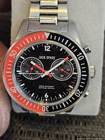 Front view of the Jack Spade men's watch showing the black dial with two subdials and bi-colored bezel in red and black.