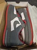 Side and top view of the black, white and red Nike Air sneakers inside the shoe box showing left and right shoes stacked on each other.