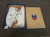 Pair of new white Champion women's sneakers with green logos inside original blue Champion box, size 6.5 with non-mark sole label.