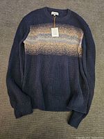 Front view of navy blue rib-knit sweater with gradient stripe pattern and attached tag.
