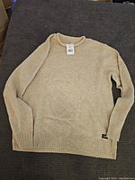 Beige knit sweater folded showing front and texture with original tags attached.