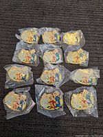 One dozen Alvin and the Chipmunks enamel pins all individually sealed in plastic bags, arranged in groups on a fabric surface.