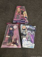 Three Bratz dolls in original packaging on carpeted surface, showing overall wear on boxes but dolls remain inside.