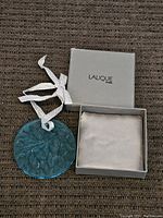 Photo of blue frosted glass Lalique ornament next to original grey Lalique Paris box with lid open.