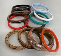 Image showing twelve bangles in a pile; includes wood, lucite, and metal bangles in various colors and patterns.
