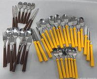 Full set arranged showing brown and yellow handled stainless steel cutlery including forks, knives, spoons, and smaller utensils all placed on gray surface