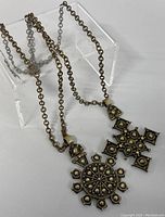 Pair of brass necklaces displayed on clear stand showing chains and pendants, confirming metal and design details.