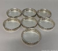 Seven Birks sterling silver coasters arranged on a flat surface, displaying their pierced ornate rims and glass inserts with etched star patterns.