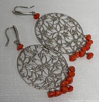 Pair of round 1.5 inch diameter silver earrings with intricate filigree floral design and red coral bead dangles. Front facing view shows design details.