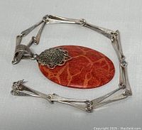 Overall view of the necklace laid flat showing the coral pendant and silver chain.