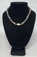 Front view of the necklace displayed on a black stand showing the full length and pearl placement.