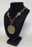 Copper necklace on black display bust, showing full view of pendant and chain with Aztec or Mayan design motifs.