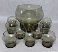 Punch bowl with 8 matching glasses arranged around it, all smoky tinted glass with black bases.