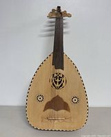 Front view of a 32-inch oud, showing pear-shaped wooden body with three sound holes and intricate rosettes, dark wooden fingerboard and tuning pegs.