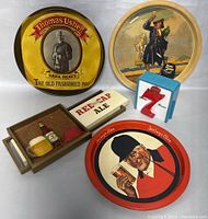 Five vintage collectible items including three tin trays, a 7-Up metal clip, and a faux drawer display with miniature beer bottle and mug