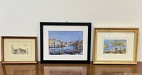 Set of three framed artworks displayed on a wooden surface showing details of each picture and frame styles.
