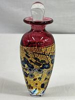 Perfume bottle front view showing red body with gold crackle glaze and multicolored accents.