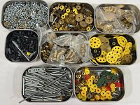 Overhead photo showing eight metal trays filled with various Meccano components such as screws, bolts, nuts, metal and plastic gears, rods, wheels, and other parts.