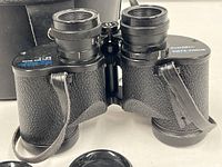 Close-up of binoculars showing textured black finish, eyepiece lenses, and focus adjustment markings marked 'Insta-Focus'. Straps attached to the binoculars and a missing eyecup visible.