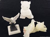 View of all three carved onyx animal figures together on black cloth background showing bear, eagle on base, and pair of doves.