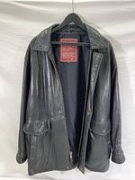 Black leather jacket hanging on a hanger, front view showing zipper undone, two flap pockets, collar, and visible red label inside.