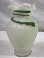 Full view of the white textured art glass vase with green vine wrapping around the body and flared ruffled rim.