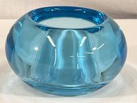 Front and side view of small thick blue glass vase with circular mouth and rounded body showing hand-blown style and clear blue hue.
