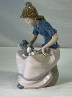 Side view of the NAO figurine showing the girl sitting with her puppies on the skirt, detailing porcelain glossy finish and painted features.