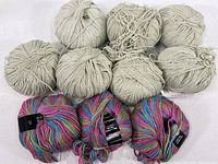Photo showing nine skeins of yarn, seven beige and two multicolor, some with tags intact.