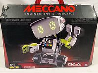 Front view of Meccano M.A.X robotic toy kit box showing image of assembled robot with LED eyes and claw hands, black and red box showing branding and caution labels.