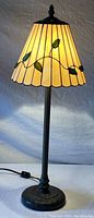 Full view of table lamp illuminated showing stained glass shade with vine motif and slender metal stand.
