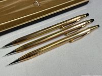 Full view of the three writing instruments (one pen, two pencils) and original box lid.