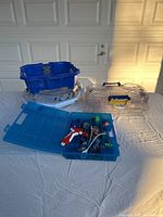 Lot overview showing three Beyblade battle arenas and blue organizer box with assorted Beyblade components on a white sheet.