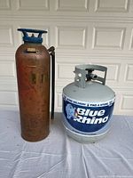 Photo of empty Blue Rhino propane tank next to antique rusty fire extinguisher with hose