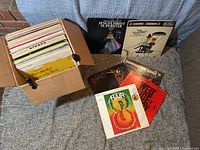 Photo of box filled with approximately 50 vinyl Broadway musical records, some records removed and displayed outside the box.