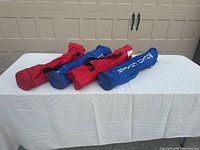 Four folded camp chairs in red and blue carry bags lying on a white table in front of a garage door.