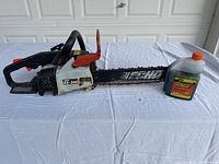 Side view of Echo CS-346 chainsaw and two stroke oil bottle on white sheet with garage background.