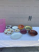 Table showing multiple decorative stoneware and pottery bowls and plates arranged in a row on a white cloth.
