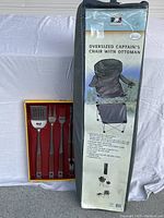 Photo showing the boxed Bobby Flay 4-piece grill tool set next to a carrying bag labeled 'Oversized Captain's Chair with Ottoman'.