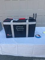 Closed carrying bag labeled Giant Tumble Tower on table in front of garage door.